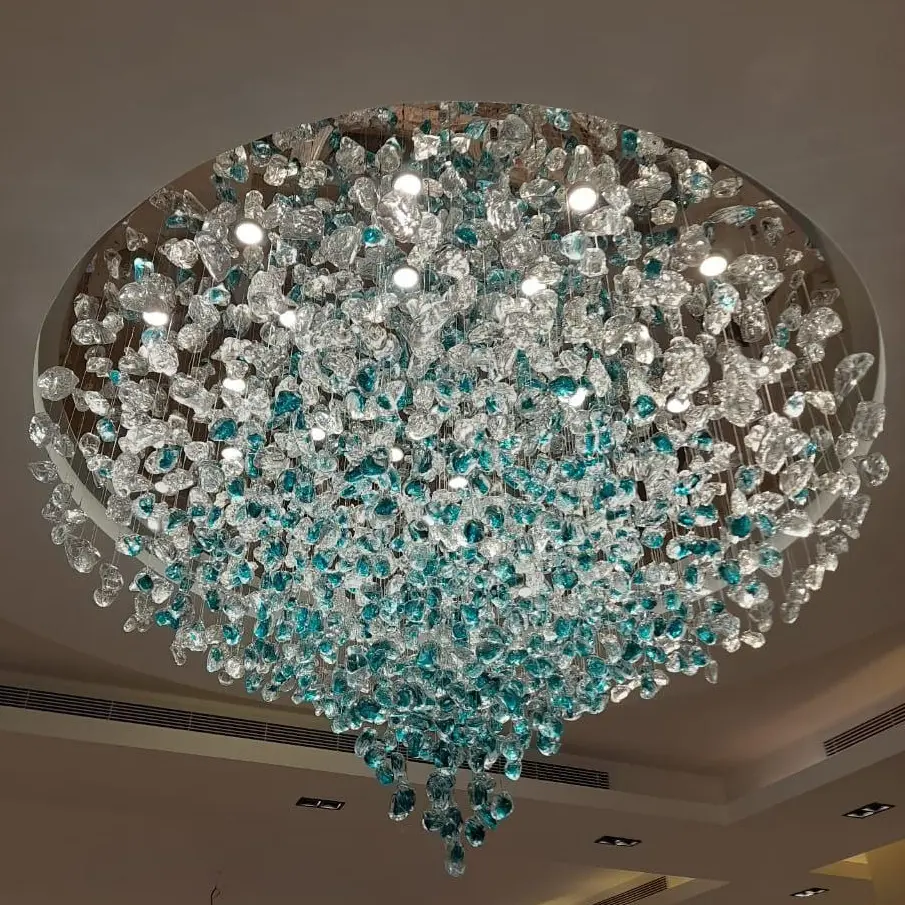 صورة لثريا كريستالية ضخمة وحديثة من نوع (Raindrop)، تم تركيبها باحترافية في سقف جبسي، تعكس إضاءة براقة بتوزيع متناسق يجمع بين الفخامة واللمسة العصرية."